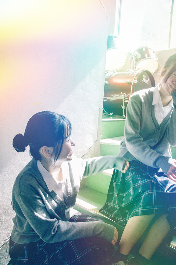 階段に座った女子生徒2人が笑いながらおしゃべりしています。
