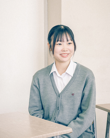 教室内の椅子に座り、笑顔でインタビューを受けているBさんの写真です