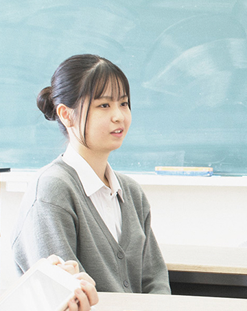 教室内の椅子に座り、笑顔でインタビューを受けているCさんの写真です