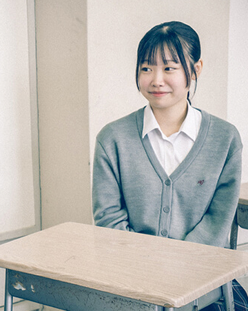 教室内の椅子に座り、笑顔でインタビューを受けているAさんの写真です