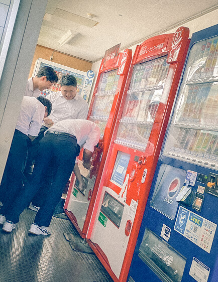 自動販売機で飲み物を買う生徒たちの写真。