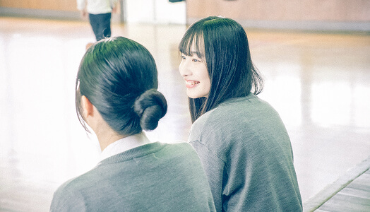 体育館で女子生徒が2人並んで話している写真です。