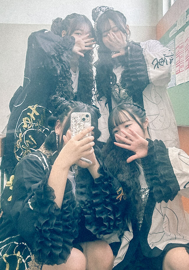 体育祭でオリジナルの衣装を着た生徒がグラウンドでしゃがんでいる写真です。