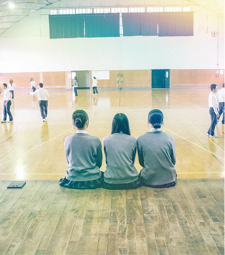 体育館のステージに3人の女子生徒が並んで座っている写真です。